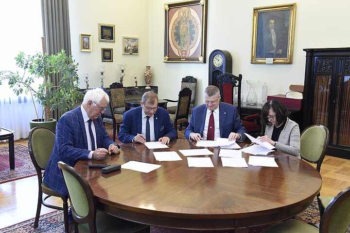 Grupa czterech osób debatuje nad dokumentem, podpisanie dokumentu i usmiechy