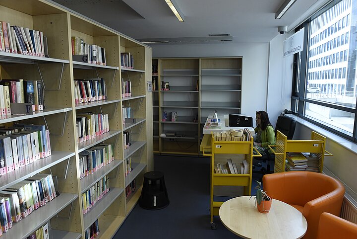 Duży rząd regałów z książkami, po prawej stronie fotele i stolik