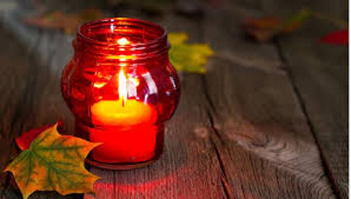 Obraz przedstawia palący się znicz nagrobny, obok leżą jesienne liście