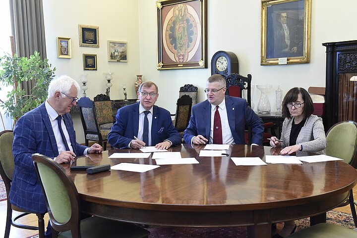 Grupa czterech osób debatuje nad dokumentem, podpisanie dokumentu i usmiechy