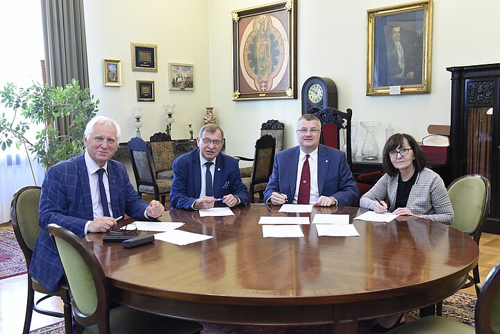 Grupa czterech osób debatuje nad dokumentem, podpisanie dokumentu i usmiechy