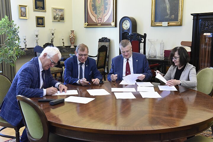 Grupa czterech osób debatuje nad dokumentem, podpisanie dokumentu i usmiechy