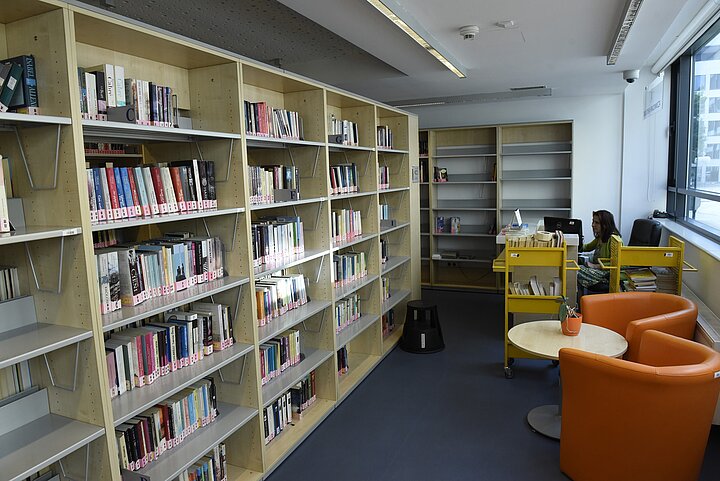 Duży rząd regałów z książkami, po prawej stronie fotele i stolik