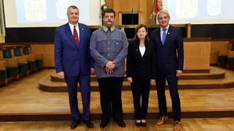 Cztery osoby stojące w sali audytoryjnej podczas uroczystości ZNP. W tle dwa ekrany z napisem ‘HONOROWYMI CZŁONKAMI ZNP’. Jedna z osób ubrana w historyczny mundur wojskowy, pozostałe w stroje formalne.”