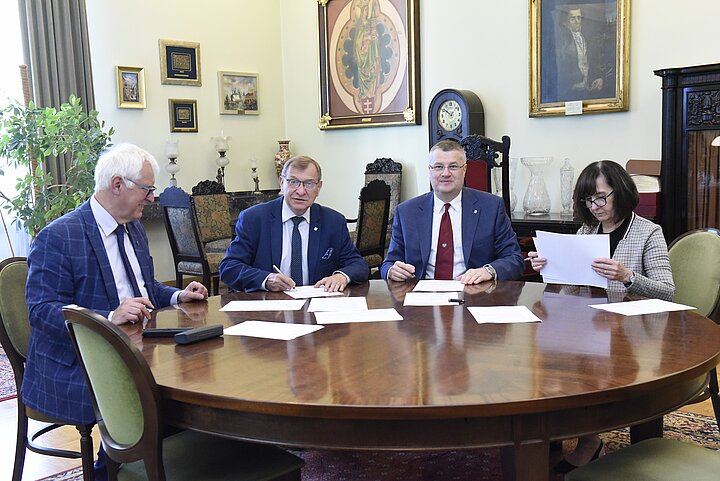 Grupa czterech osób debatuje nad dokumentem, podpisanie dokumentu i usmiechy