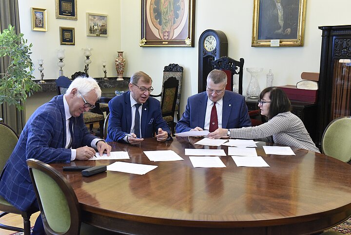 Grupa czterech osób debatuje nad dokumentem, podpisanie dokumentu i usmiechy