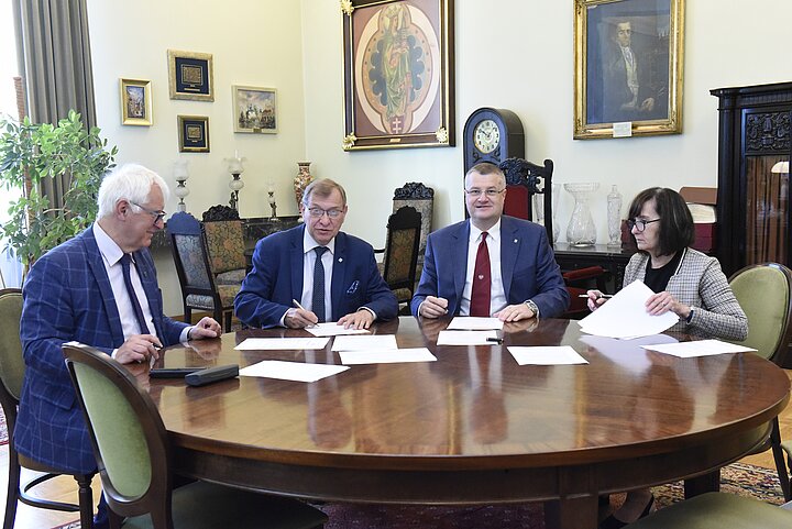 Grupa czterech osób debatuje nad dokumentem, podpisanie dokumentu i usmiechy