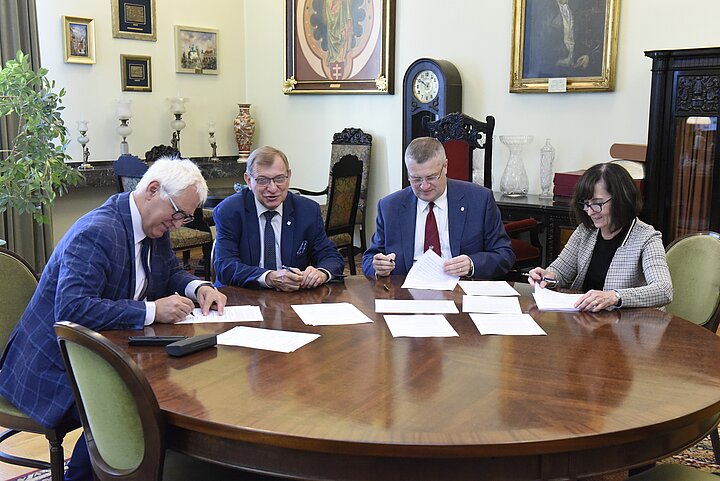 Grupa czterech osób debatuje nad dokumentem, podpisanie dokumentu i usmiechy