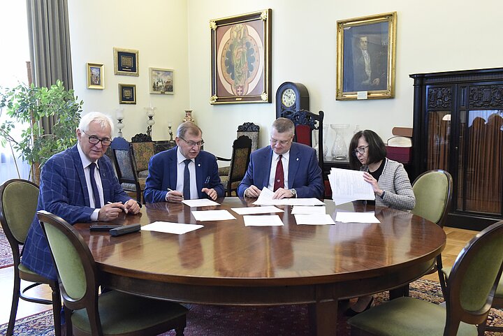Grupa czterech osób debatuje nad dokumentem, podpisanie dokumentu i usmiechy