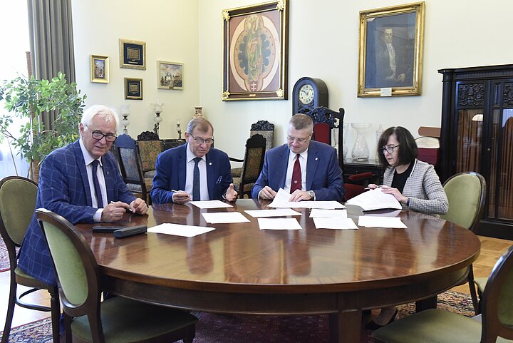 Grupa czterech osób debatuje nad dokumentem, podpisanie dokumentu i usmiechy